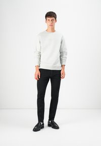 Light gray sweatshirt with ribbed cuffs and hem, paired with black slim-fit jeans. Model wears black loafers. Minimalistic design, plain colors.
