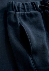 Marineblå sweatpants med en blød tekstur, der har en elastisk talje og en sidelomme. Stoffet ser glat og lidt tykt ud.