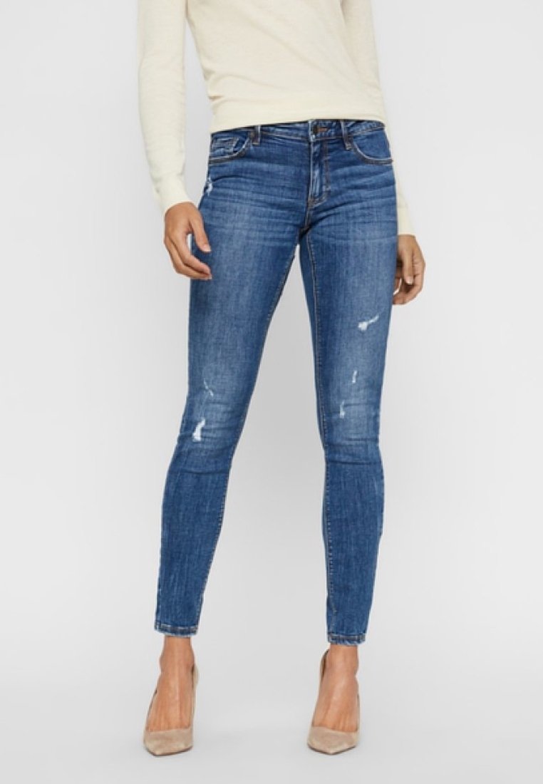 Slim-fit jeans i medelblå denim, med slitna lappar och midjehöjd. Kombineras med nakna högklackade skor.