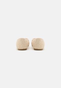 Neulottu kangasvarvas, vaaleanbeige väri, pyöreä kärki ja minimalistinen muotoilu. Pohja on tasainen ja valmistettu kevyistä materiaaleista.