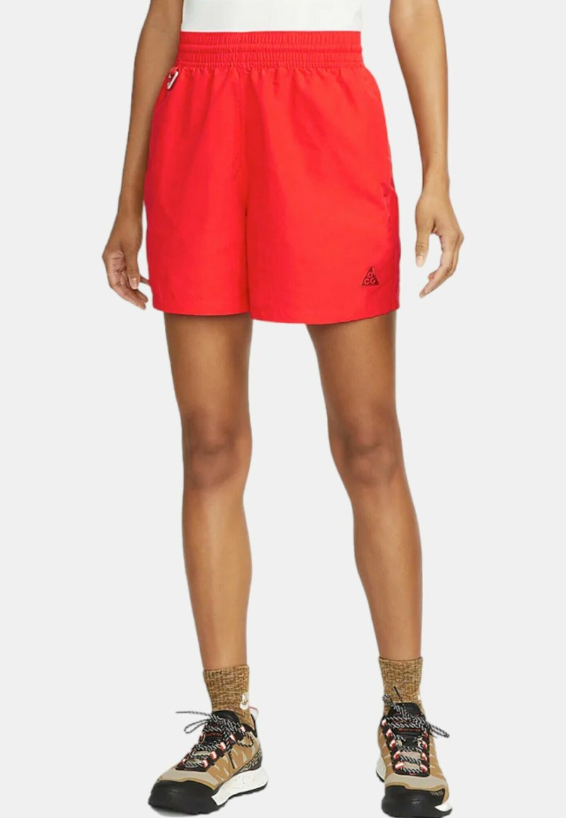 Röda shorts med elastisk midjeband, med sidofickor och en liten svart logotyp. Materialet verkar lätt och glatt.