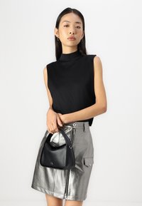 Top negru fără mâneci, fustă metalică argintie și geantă mică neagră. Texturi netede cu fermoar în față și buzunare laterale pe fustă.