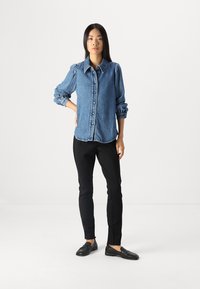 Blue denim shirt with puffed sleeves and a button front, paired with black fitted pants and black slip-on shoes. Simple and structured design.