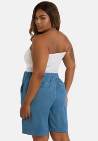 Ljust blå shorts med avslappnad passform, elastisk midja, sidofickor och en slät yta. Bärs med en vit strapless topp.