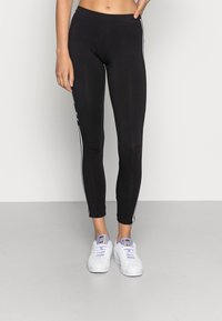 Leggings neri realizzati in tessuto elasticizzato, con strisce bianche sui lati e un design aderente. Abbinati a sneakers bianche.