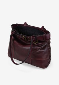 Bolso de mano de cuero burdeos oscuro con asas dobles, cierre superior con cremallera y detalles de hebilla de latón, presentado abierto con un forro interior de tela negra.