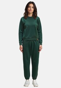 Groene sweatshirt en broek set, gemaakt van zachte stof. Crewneck ontwerp met elastische manchetten en een trekkoord in de taille. Witte sneakers erbij.