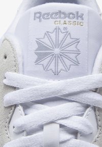 Weißer Sneaker mit Obermaterial aus Wildleder und Textil, Reebok-Logo in Hellgrau und Gold, runden Schnürsenkeln und gepolsterter Zunge mit Emblem.