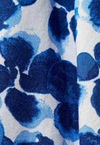 Tissu blanc avec des taches abstraites bleues et bleu marine ressemblant à des motifs de peinture à l'aquarelle, montrant la texture et de légers plis.