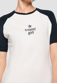 Biała koszulka z granatowymi rękawami raglanowymi, z haftowanym napisem "tommy girl" oraz małą gwiazdką powyżej. Wykonana z bawełny, z okrągłym dekoltem.