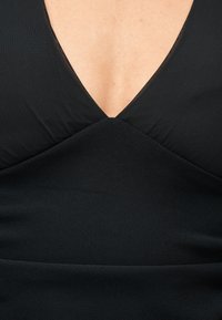 Κοντινό πλάνο ενός ατόμου που φοράει μαύρο ρούχο με V-λαιμόκοψη, υφασμένο με υφή και βαθύ ντεκολτέ που αφήνει την επιδερμίδα ορατή.