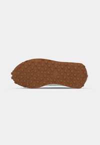 Semelle en caoutchouc marron avec motif à carreaux, partie visible de la tige grise de la chaussure sur fond blanc.