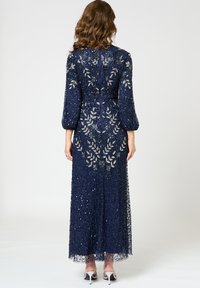 Marinblå aftonklänning i spets med paljetterade blommönster, trekvartslånga puffärmar och dragkedja bak.