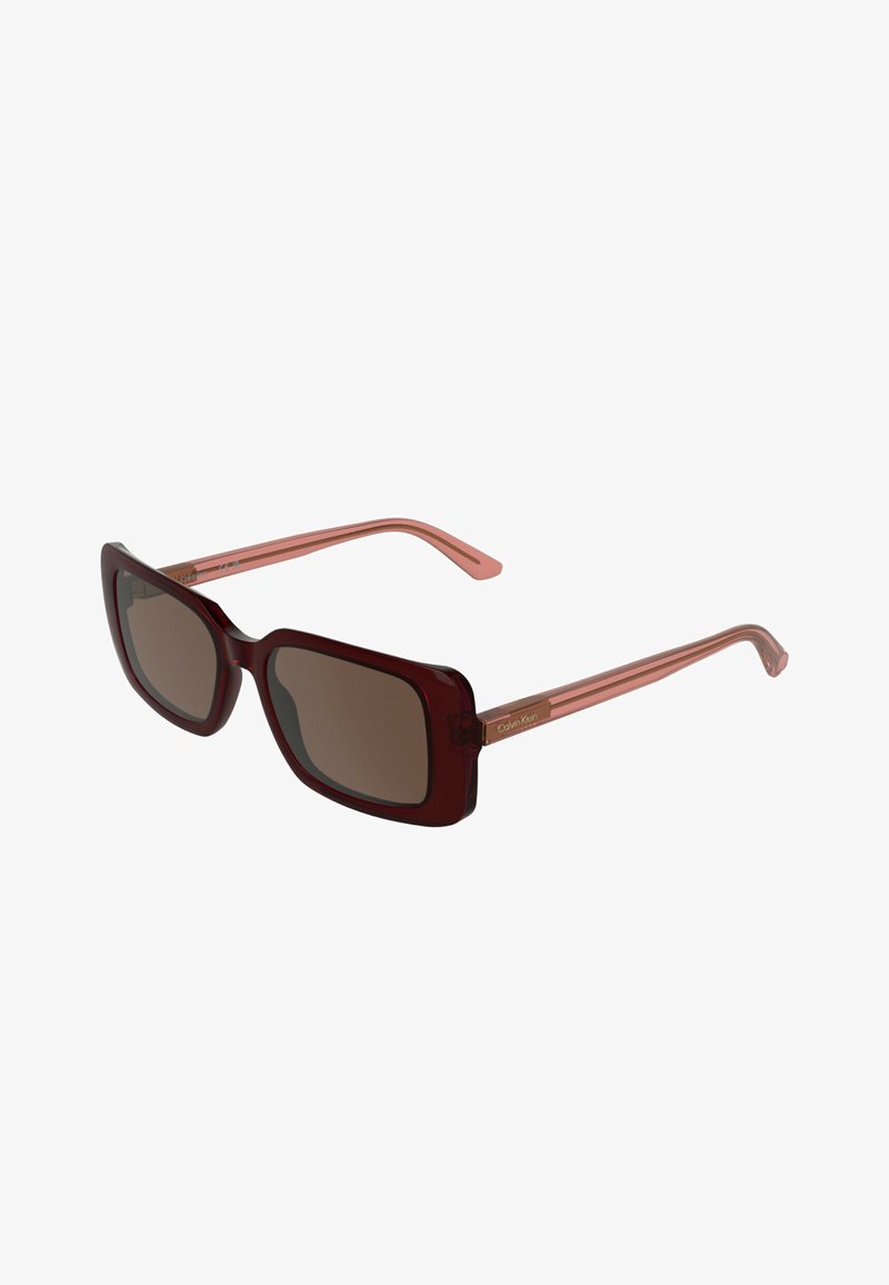 Verres rectangulaires brun foncé avec montures et branches translucides brun rougeâtre, ornés d'un petit logo Calvin Klein sur les branches.