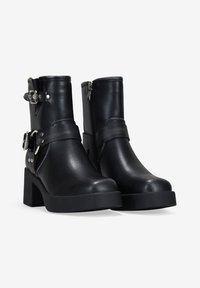 Botines negros de piel lisa con tacones de bloque, que cuentan con correas ajustables y detalles en metal plateado. Cierre con cremallera en la parte trasera.