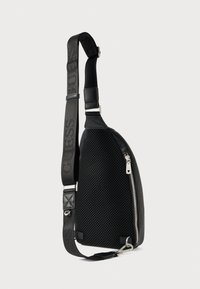 Czarna torba na ramię z siateczkową teksturą, elegancki design, srebrny zamek błyskawiczny oraz regulowany pasek z wytłoczonym nazwiskiem marki.