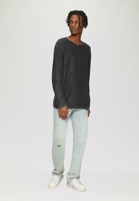 Donkergrijze longsleeve shirt met een ronde hals, gecombineerd met lichtblauwe jeans met een scheur op de knie en witte sneakers.