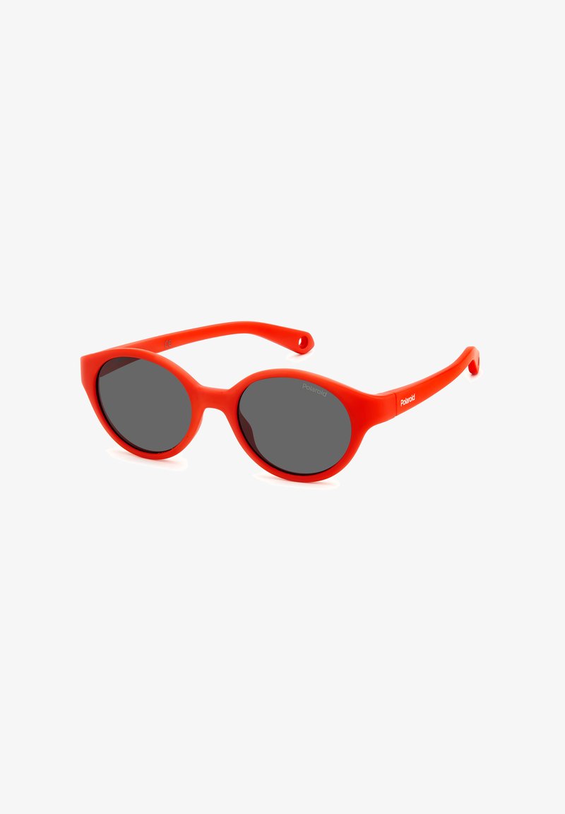 Lunettes de soleil en plastique rouge avec une finition mate, verres ovales et verres teintés en gris foncé. Elles présentent un pont courbé et des branches flexibles.