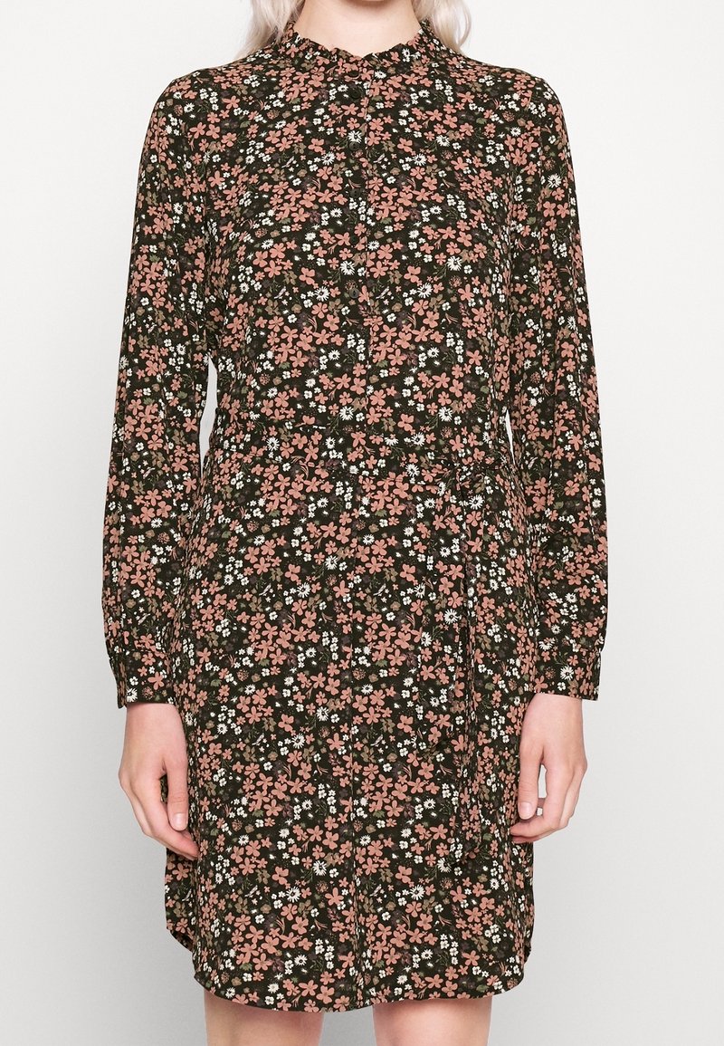 Robe à manches longues boutonnée à motif floral avec des fleurs roses et blanches sur fond vert foncé, portée par une personne montrée du cou aux genoux.