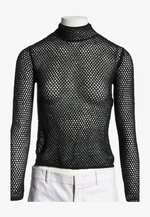 Haut noir en maille à manches longues avec col montant présenté sur un mannequin, associé à un pantalon blanc à la taille.