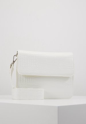 Biała torebka na ramię z eko skóry krokodyla z klapką i odpinanym paskiem, na białej powierzchni na jednolitym tle.