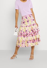 Kukkalinen kerroksellinen hame vaaleanpunaisissa, keltaisissa ja purppuran sävyissä, valmistettu kevyestä kankaasta. Yhdistetty liilaan T-paitaan ja valkoiseen käsilaukkuun.