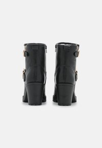 Botas negras de tobillo con acabado de cuero suave, tacones gruesos, cremalleras laterales y hebillas en tono dorado a cada lado.