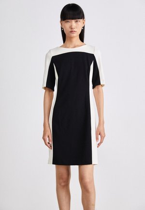 Robe à manches courtes présentant un corps noir avec des panneaux latéraux blancs, un col rond et une silhouette ajustée. Tissu lisse avec un minimum de détails.