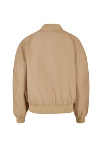 Giacca bomber beige con colletto e polsini a coste, orlo elasticizzato e texture liscia. Presenta una vestibilità morbida e un design semplice.