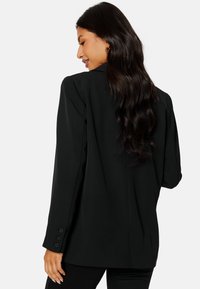Czarna marynarka wykonana z gładkiego materiału o dopasowanym kroju. Posiada trzy guziki na każdym mankiecie oraz jeden rozcięcie z tyłu, co zapewnia swobodę ruchów.