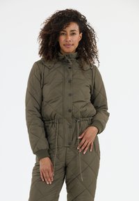 Vuorattu, oliivinvihreä tyynyjäkt, jossa on korkea kaulus, etupainikkeet ja kiristettävä vyötärö. Ribattuja hihansuita ja taskut sivuilla.