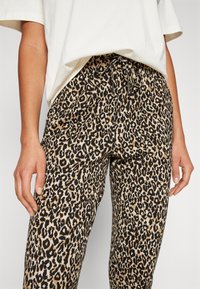 Pantalons à imprimé léopard présentant un motif beige et noir, avec une taille à cordon de serrage et une coupe décontractée. Texture de tissu lisse.