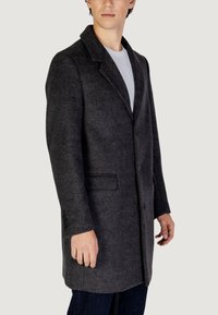 Abrigo de lana gris con cuello de muesca, dos bolsillos frontales y puños abotonados, exhibido en un modelo sobre un fondo neutro.