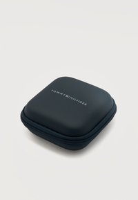 Μικρή μαύρη θήκη με φερμουάρ, με το λογότυπο Tommy Hilfiger στο κέντρο στην κορυφή, τοποθετημένη σε απλό λευκό φόντο.