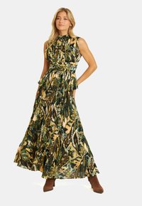 Abito lungo con scollatura alta, motivo astratto verde e oro, vita arricciata e gonna fluida, abbinato a stivali alla caviglia marroni.