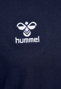 Weiß besticktes hummel-Logo und Text auf dunkelblauem Stoffhintergrund, zentriert auf dem Kleidungsstück.