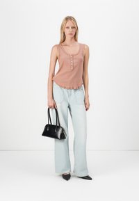 Lichtroze geribbeld mouwloos shirt met knoopdetail, gecombineerd met lichtblauwe wijde jeans. Een zwarte handtas en puntige zwarte schoenen maken de look compleet.