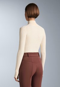 Kremasti rebrasti pulover s visokim ovratom, uparen s uskim tamnosmešim hlačama sa strukturiranim pojasom i ukrasnim šavovima.