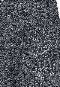 Marinblått mönstrat tyg med intrikata vita blommiga och spiralformade mönster, med en liten logotypaccents near midjan.