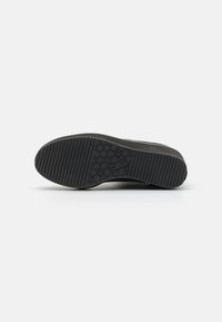 Semelle de sneaker noire avec un motif de grip texturé, présentant des formes horizontales et circulaires. Fabriquée en caoutchouc pour la durabilité et l'adhérence.