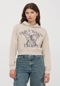 Beżowy krótki hoodie z graficznym motywem duszka z przodu oraz napisem "NIE MARNUJ ENERGII." Posiada sznurki do regulacji i ściągacze przy mankietach.