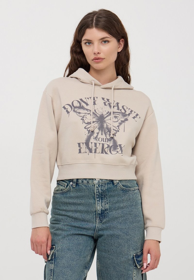 Beżowy krótki hoodie z graficznym motywem duszka z przodu oraz napisem "NIE MARNUJ ENERGII." Posiada sznurki do regulacji i ściągacze przy mankietach.