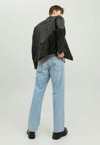 Chaqueta de cuero negra de motorista con superficie texturizada, combinada con jeans de denim de pierna ancha en azul claro y botas negras robustas, vista desde atrás.
