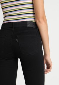 Jeans de mezclilla negra con una silueta ajustada, que cuentan con bolsillos traseros y un parche de logo de cuero texturizado negro en la cinturilla.