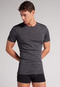 T-shirt z krótkim rękawem w ciemnoszarym kolorze, wykonany z miękkiej i elastycznej tkaniny. Okrągły dekolt i slim fit nadają luźny wygląd. Widoczne czarne bokserki.