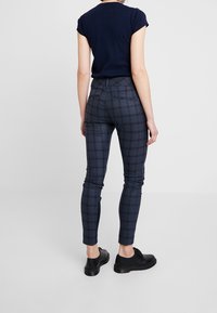 Marinblå rutiga smala byxor med borstad yta, med hög midja, två bakfickor och uppvikta anklar, kombinerade med svarta skor.