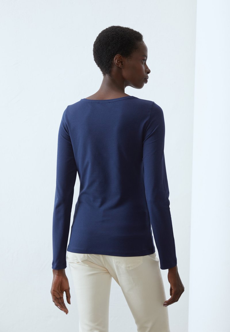 Maglietta a maniche lunghe navy in cotone texture, con scollo rotondo e una silhouette semplice e snella, abbinata a pantaloni chiari.
