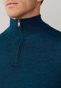 Ciemnoniebieski sweter zapinany na zamek z wysokim kołnierzem. Posiada fakturowany materiał oraz małe haftowane logo po lewej stronie klatki piersiowej.