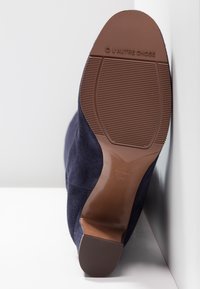 Stivale alla caviglia in suede blu navy con suola in gomma e motivo testurizzato, caratterizzato da un tacco curvo e da un marchio impresso sulla suola.