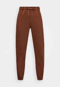 Bruna sweatpants med dragsko i midjan, sidfickor och kontrasterande gula stygn längs sömmarna. Tyget är mjukt och något texturerat.